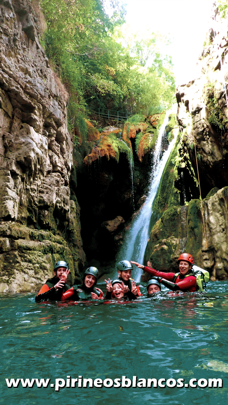 Participantes equipados con neopreno y casco posando felices en una poza cristalina bajo una cascada, en el Barranco del Viandico, una ruta clásica de barranquismo en el entorno de Ordesa y el Cañón de Añisclo con guías de Pirineos Blancos